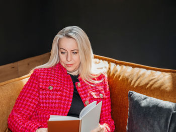 Mature lady engrossed in a novel, relaxed on a mustard couch