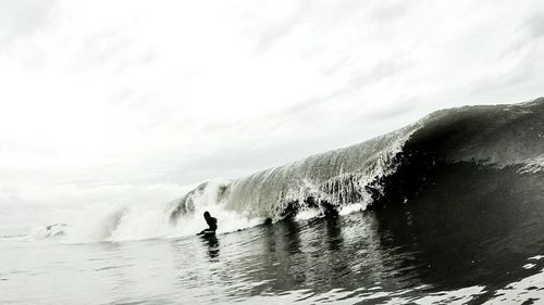 Man surfing with wave in sea against sky