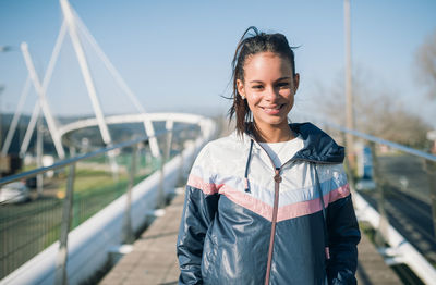 Young woman in jacket standing on footbridge against sky