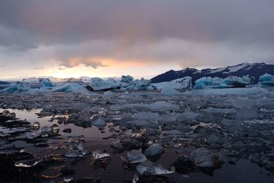 Scenic view of frozen lake against cloudy sky during sunset