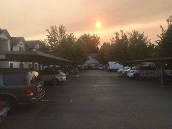 Cars on street by houses against sky at sunset