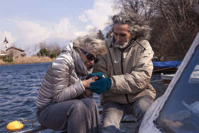 Beautiful mature couple having fun sitting on a original boat on the lake in a winter day