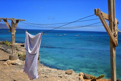 Clothes drying on wooden post at beach against blue sky