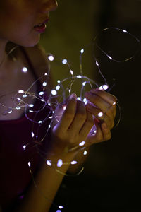 Woman holding illuminated string light in darkroom