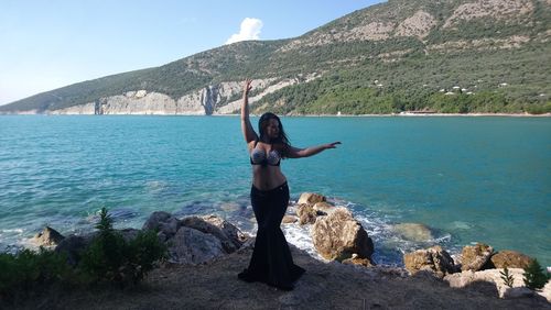 Young woman dancing by sea and mountain against sky