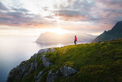 Rear view of man walking on mountain against sky during sunset