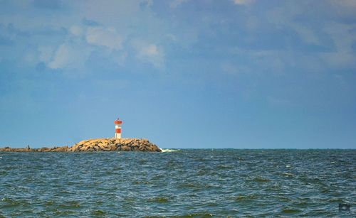 Lighthouse by sea against blue sky