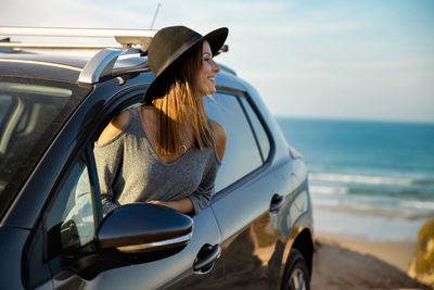 Woman looking away while sitting in car at beach during sunset