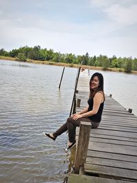 Portrait of woman sitting by lake against sky