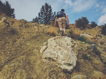 Low angle view of man climbing on mountain against sky