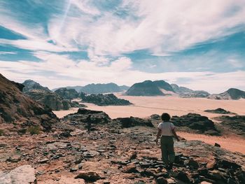 Rear view of man standing on rock against sky