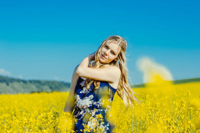 Young woman with yellow flower on field against blue sky
