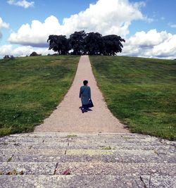 Rear view of woman sitting on footpath against sky