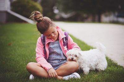 Full length of girl sitting with dog on grassy field