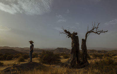 Rear view of woman standing on field against sky during sunset