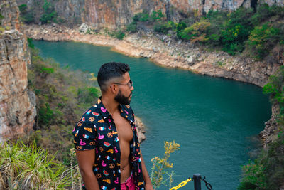 Young man wearing sunglasses standing against river