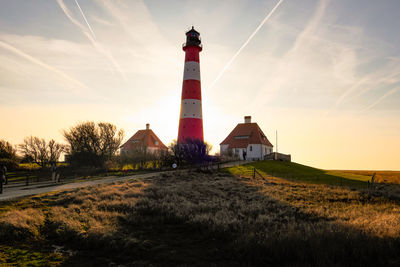 Lighthouse on field by building against sky at sunset