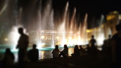 Silhouette people standing at illuminated city against sky at night