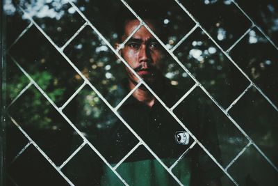 Portrait of young man with umbrella seen through rain