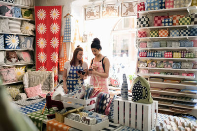 Female owners using smart phone and digital tablet while standing in fabric shop