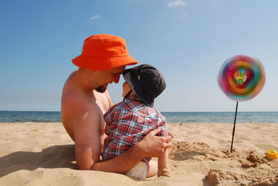 Smiling shirtless father looking at son on sandy beach