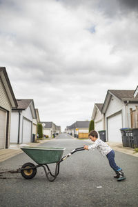 Young boy pushing wheelbarrow in back alley.