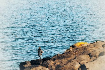 High angle view of man standing on rock by sea