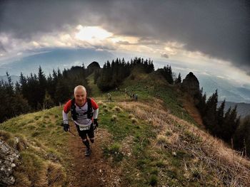 High angle view of man hiking on mountain against cloudy sky