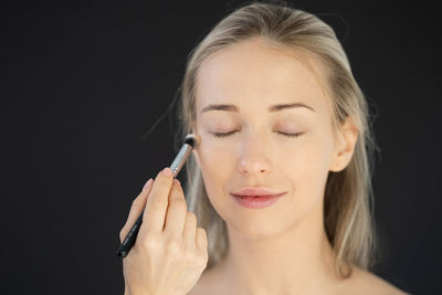 Portrait of young woman holding face against black background