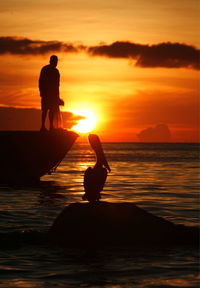 Silhouette of people standing on beach at sunset