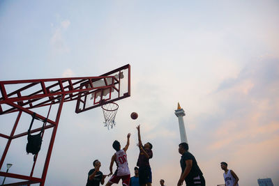 Low angle view of people playing basketball against sky during sunset