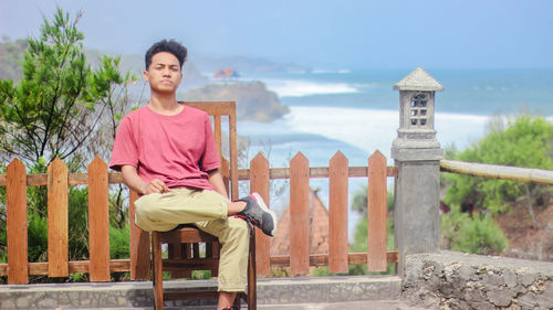 Portrait of young man sitting on chair against sea
