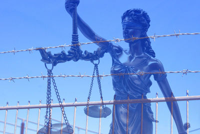 Double exposure of lady justice statue and fence against clear blue sky