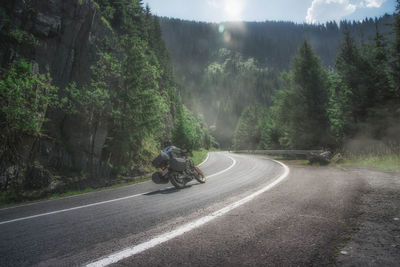 People riding motorcycle on road amidst trees against sky