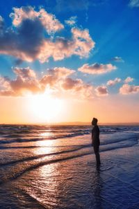 Silhouette woman standing at beach against sky during sunset