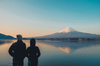 Rear view of friends looking at mt fuji while standing by lake against clear sky