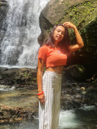 Full length of smiling woman standing against waterfall