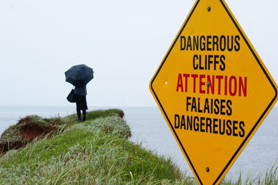 Warning sign with person in background against clear sky