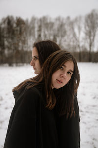 Portrait of young woman standing with friend on snow outdoors