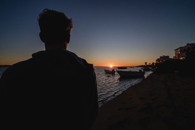 Rear view of silhouette man on beach against clear sky