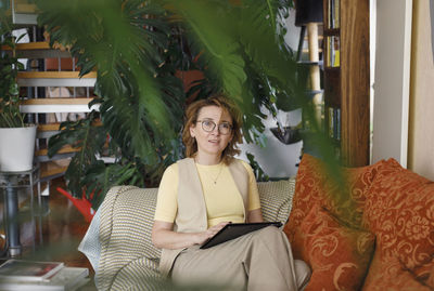 Redhead businesswoman with digital tablet sitting on sofa at home