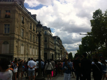 People walking on city street against cloudy sky