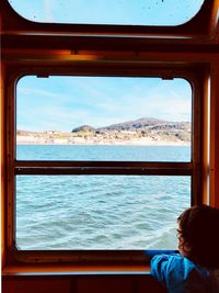 Rear view of boy looking at sea seen through window