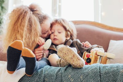 Girl kissing cute brother on sofa at home