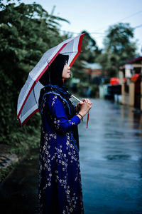 Rear view of woman with umbrella standing in city