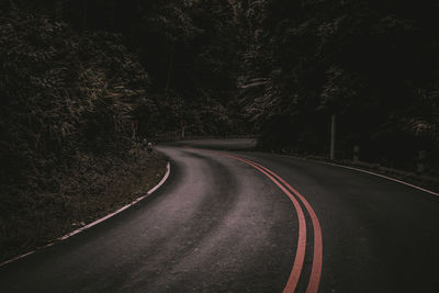 Empty road along trees at night