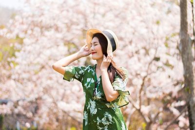 Smiling woman wearing sun hat while standing against trees