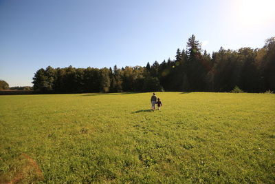 Rear view of sisters walking on grassy field against trees