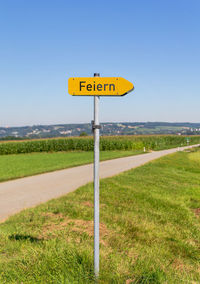 Road sign on field against clear sky