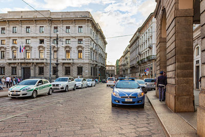 Cars on street by buildings against sky in city